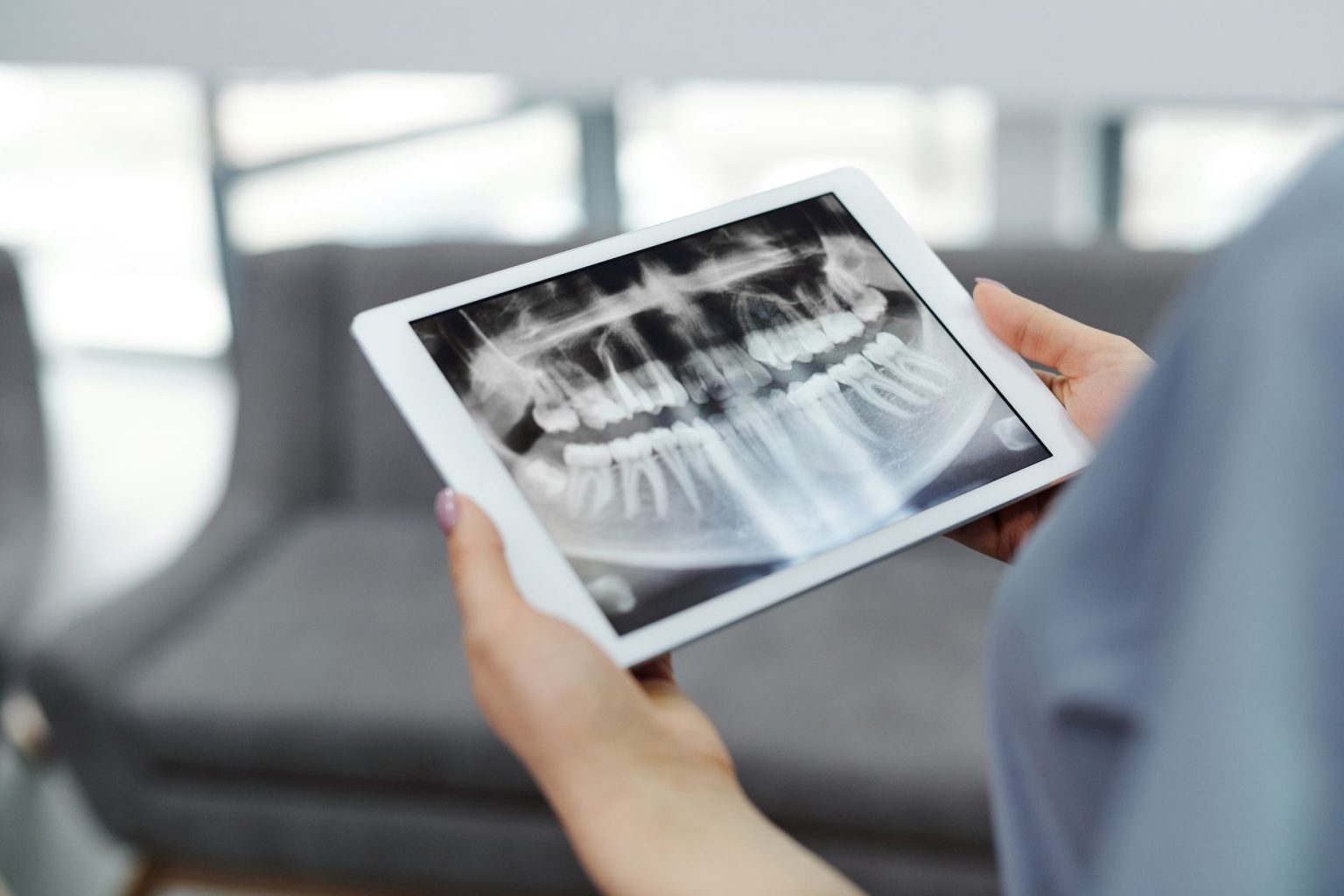 Hands holding a tablet that shows a panoramic dental X-ray
